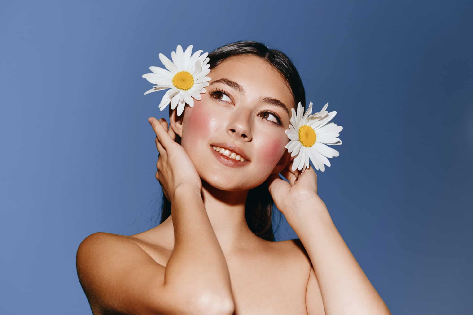 Smiling young woman with daisy flowers in her hair on a blue background
