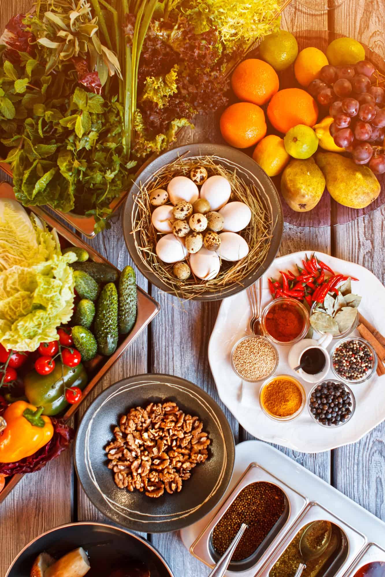 Top view of fresh vegetables, fruits, spices, nuts, and eggs arranged on a wooden table
