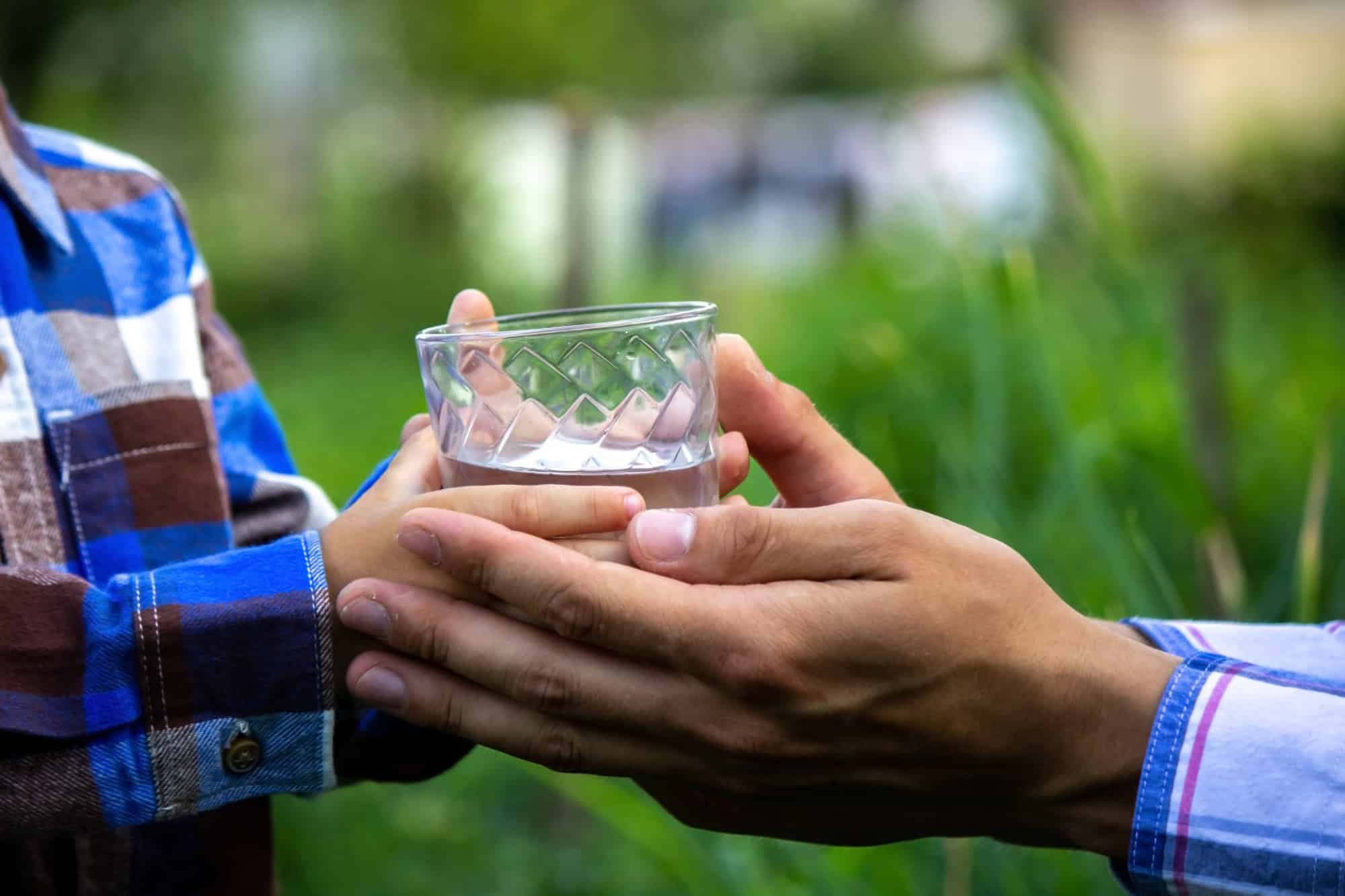 Close-up of two people passing a glass of water between hands in a caring gesture outdoors