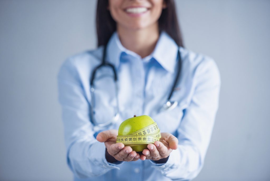 Smiling doctor holding a green apple wrapped in measuring tape, symbolizing weight loss and healthy nutrition