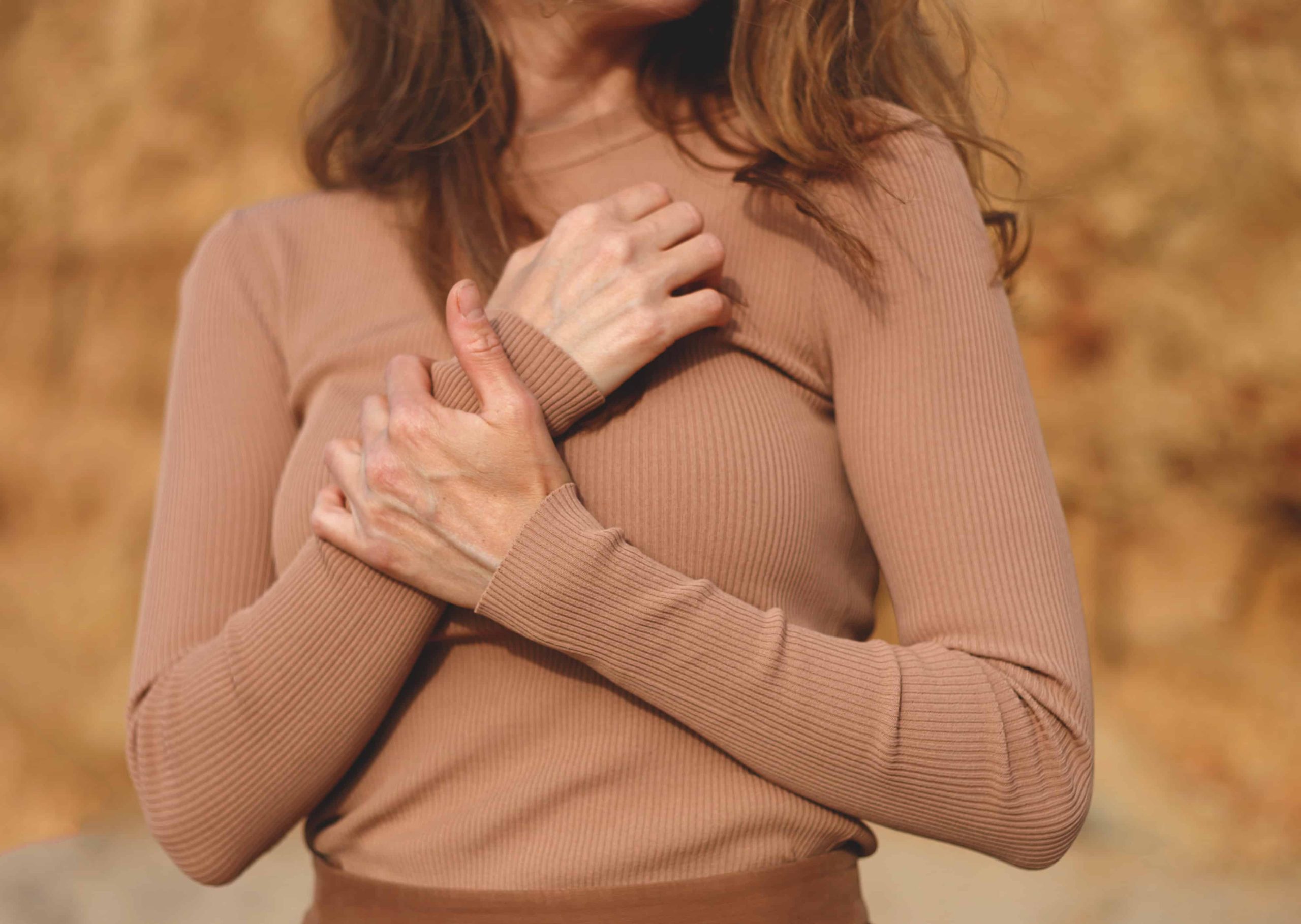 Close-up of a woman gently holding her chest in a comforting gesture, wearing a beige top