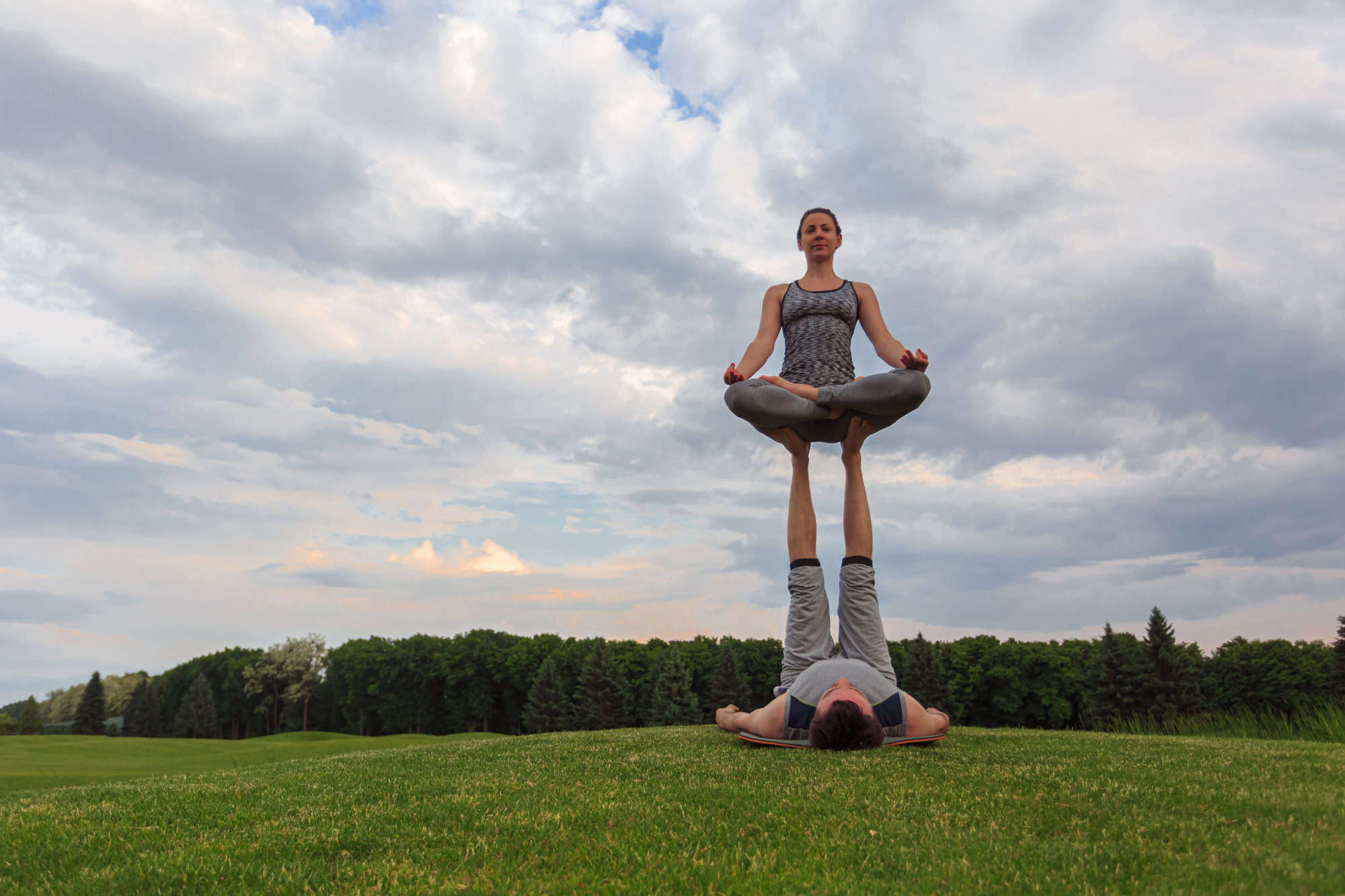 Man and woman performing a balancing yoga pose outdoors, symbolising HueLight’s holistic approach to energy alignment and body balance.