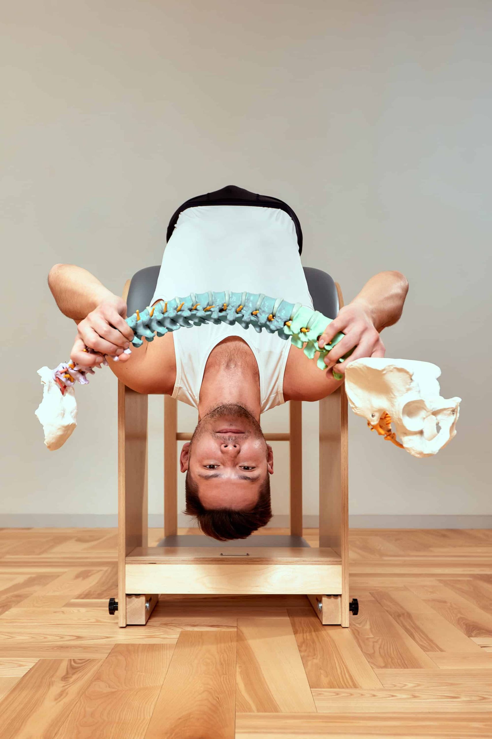 Man lying inverted while holding a spine model, symbolising spinal decompression, realignment, and nervous system optimisation.