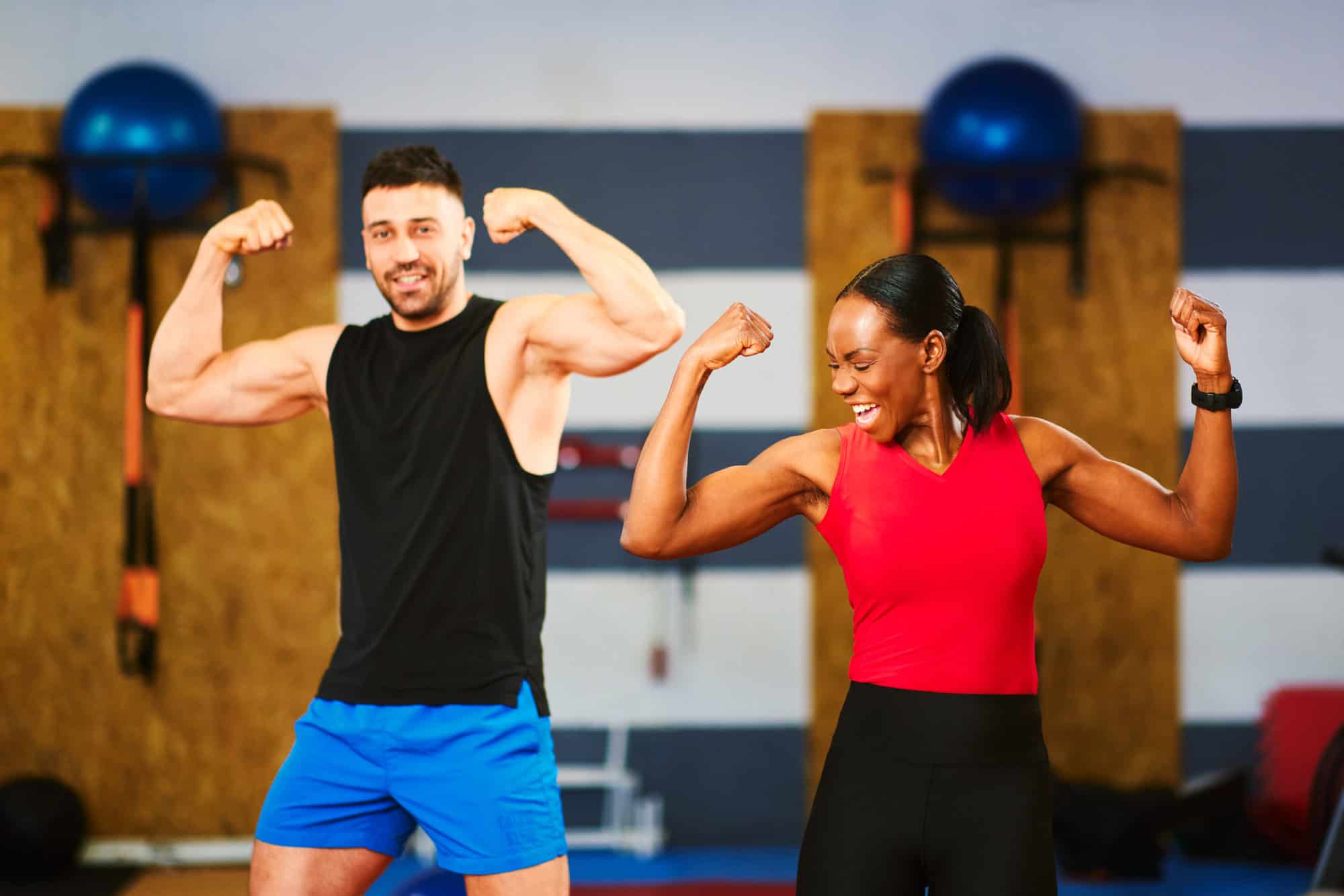 Fit man and woman flexing muscles and smiling in a gym, symbolising HueLight therapy for energy, strength and recovery.